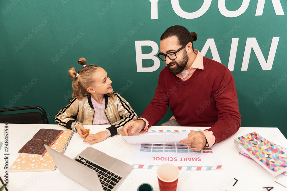 Fototapeta premium Cute fair-haired girl with bracelets on her hand smiling to her teacher