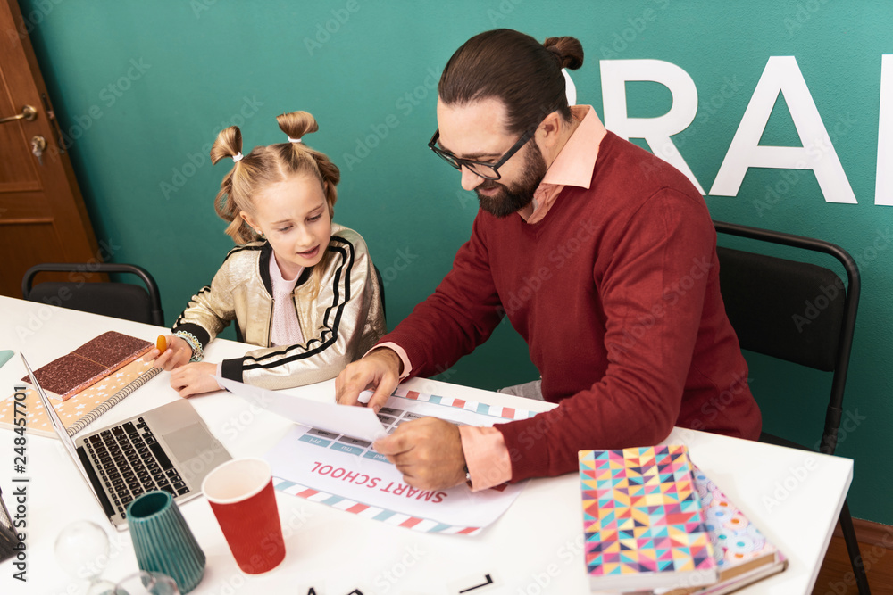 Fototapeta premium Dark-haired bearded smiling teacher showing pictures to his pupil