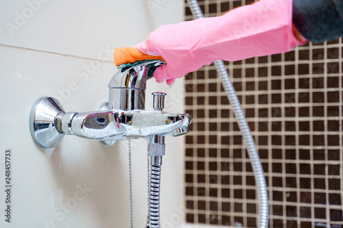 Picture of woman's hands in pink rubber gloves washing bathtub mixer