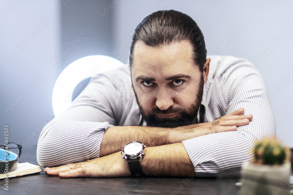 Obraz premium Dark-haired bearded man in a striped shirt feeling tired