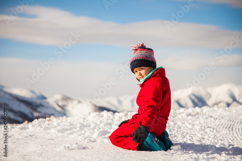 Portrait of happy little girl playing on the top of mount with ice and snow