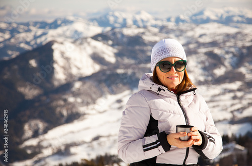 Adult woman with thermos on mount top with spectacular view of snowy mountains on background