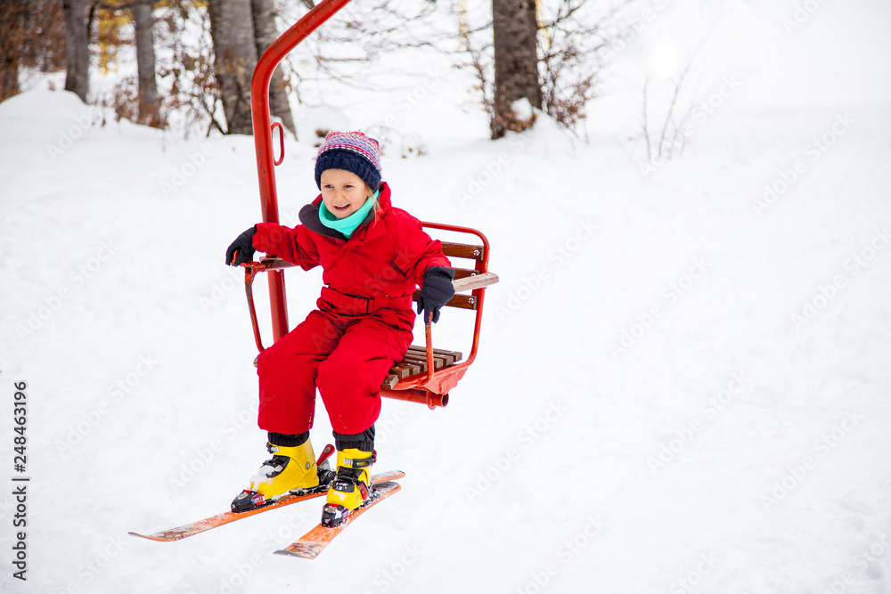Little girl in red overall using chairlift with her skies