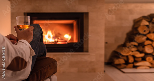 Man sitting at home by the fireplace and drinking a whiskey. 