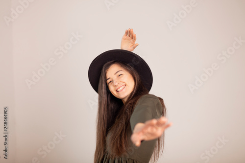 Young sensual caucasian woman in dark green (olive) dress holding fedora hat isolated on white-grey background with beautifull smile © Максим Галінский