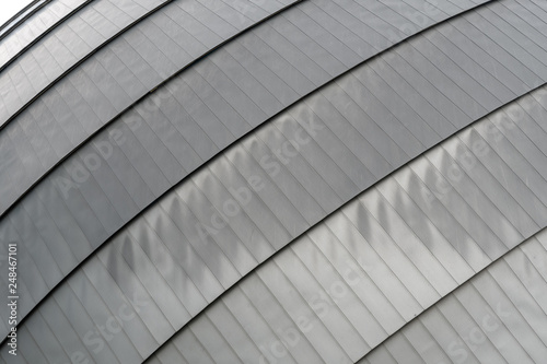 Metallic roof top with rounded lines in urban environment, dark grey, suitable as background