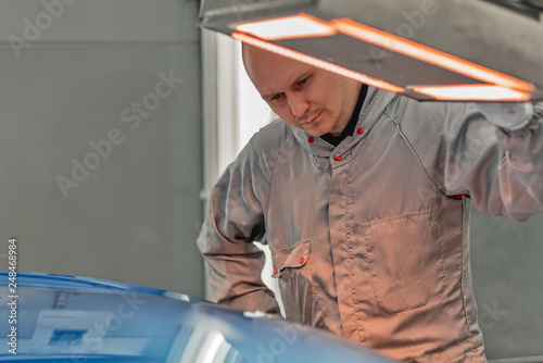 The worker of shop of coloring carries out drying of a varnish by means of a special lamp