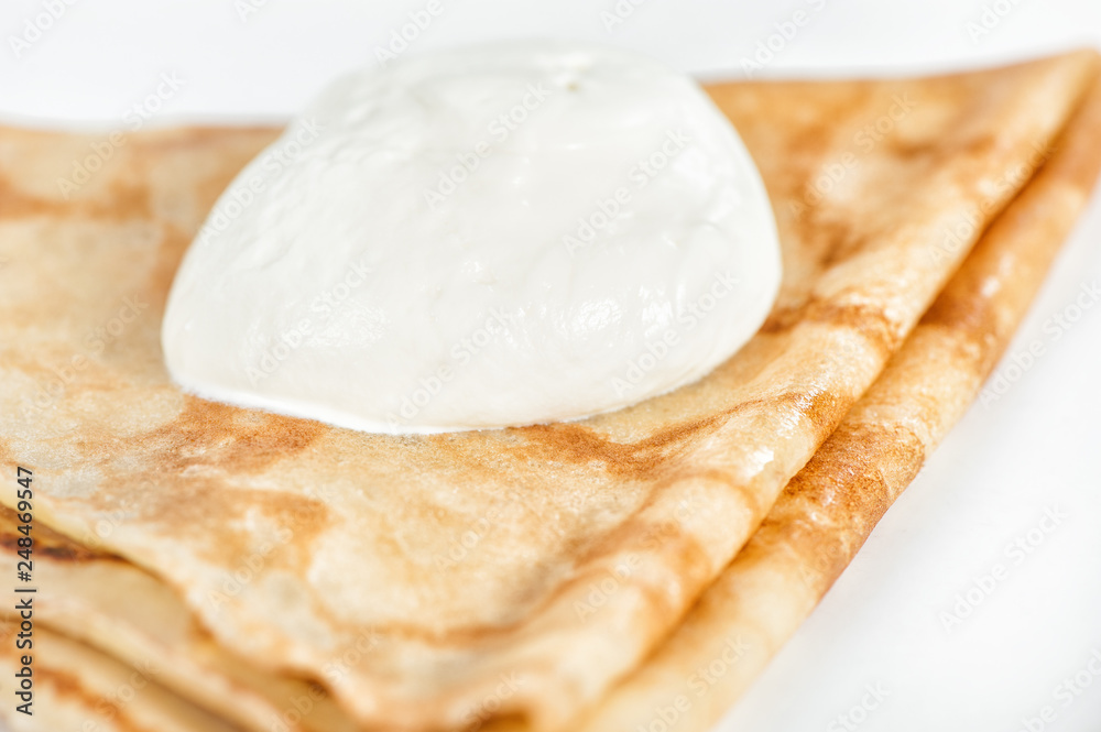 Thin delicious pancake with sour cream on white