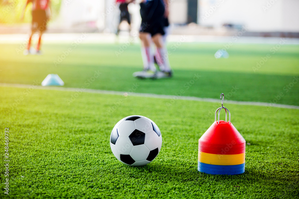 Soccer ball and cone marker on green artificial turf with blurry of soccer player training