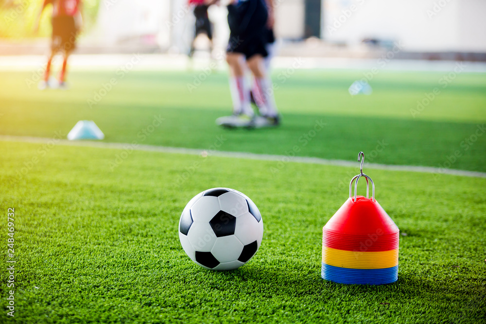 Soccer ball and cone marker on green artificial turf with blurry of soccer player training Soccer ball and cone marker on green artificial turf with blurry of soccer player training
