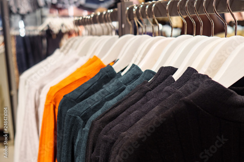 Rack with hangers of various colorful sweaters for sale in modern clothes store