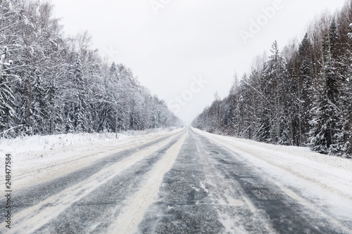 winter road with ice on the asphalt, trees under snow during the winter frost in Russia