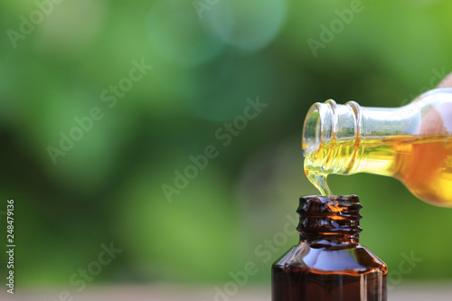Fototapeta Naklejka Na Ścianę i Meble -  Woman hand holding essential oil or vitamin C to the bottle on natural green background, Cosmetic pipette and spa concept