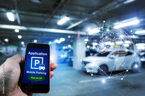 Pick me up, mobile smart phone in hand using application for intelligent car park with digital hologram on blurred parking car background, mobile auto parking, network and online technology concept