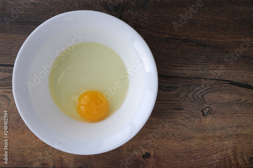 raw egg without shell in a white plate on a wooden board background