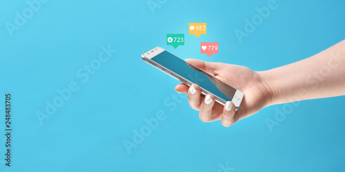Girl's hand holding smartphone in hand, surrounded with social media notification icons on blue background