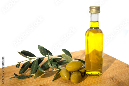 Glassy bottle of olive oil with group of green shiny olives and brunches with leafs