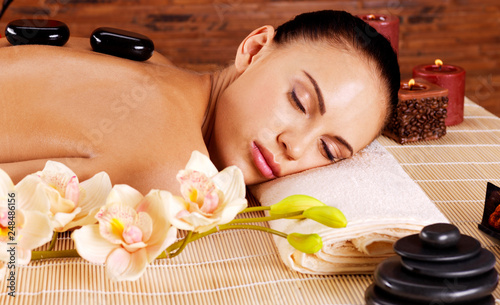 Adult woman relaxing in spa salon with hot stones on back