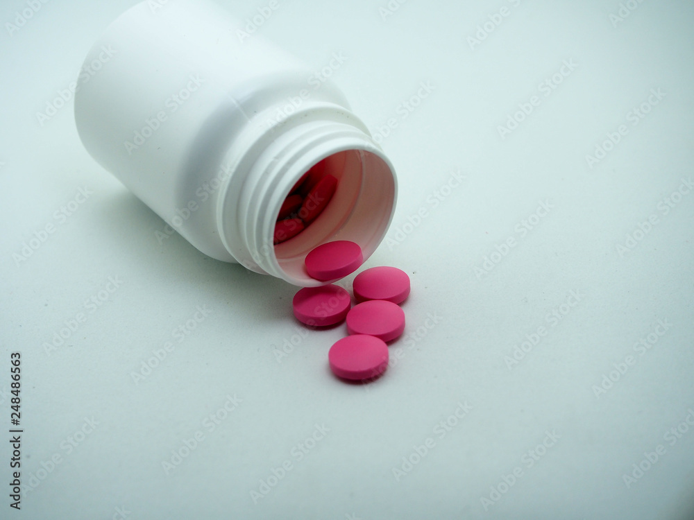 Red tablets are poured from a white plastic jar. Red tablets are poured from a white plastic jar.