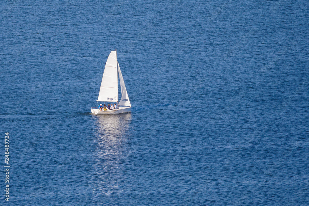 Fototapeta premium A small white sailing ship on the blue water with reflection (copy space)