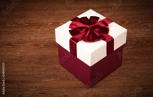 white box with red bow on a wooden background © mizar_21984