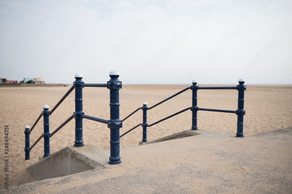 A rustic metal seaside bannister railing against a sandy beach backdrop. railings saves lives at the seaside. vintage seaside architecture. A rustic metal seaside bannister railing against a sandy beach backdrop. railings saves lives at the seaside. vintage seaside architecture.