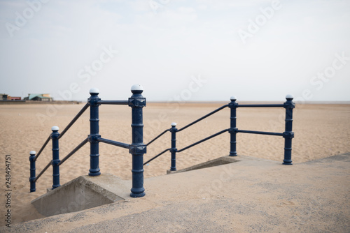 A rustic metal seaside bannister railing against a sandy beach backdrop. railings saves lives at the seaside. vintage seaside architecture.