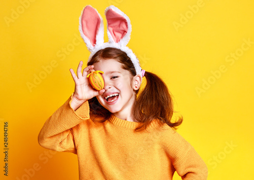 funny happy child girl with easter eggs and bunny ears on yellow