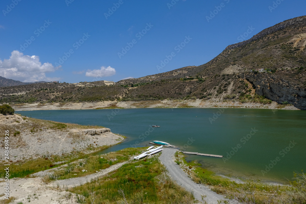 View of the germasogeia dam in Cyprus, taken on a bright blue sky day. Shot shows a path leading to canoes at the side of the vividly blue green lake.