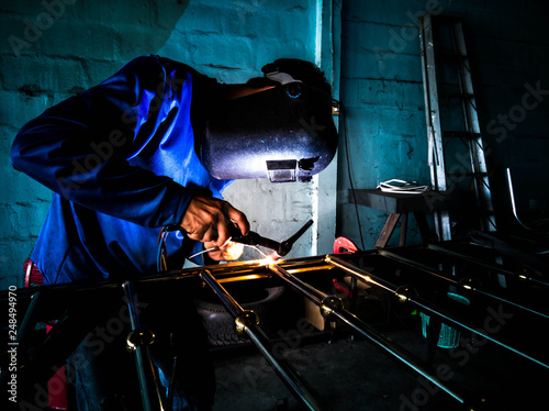 Picture of mechanic welding aluminum door with electric welding machine.