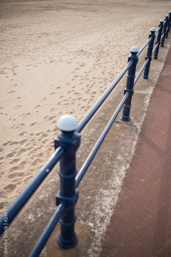 A rustic metal seaside bannister railing against a sandy beach backdrop. railings saves lives at the seaside. vintage seaside architecture. A rustic metal seaside bannister railing against a sandy beach backdrop. railings saves lives at the seaside. vintage seaside architecture.