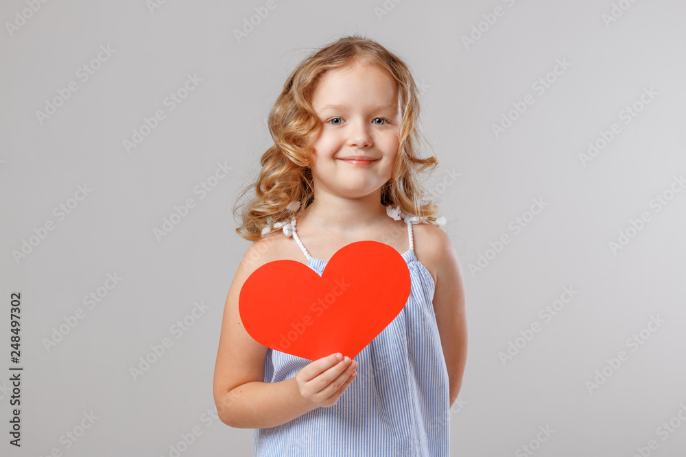Portrait of an adorable little child girl holding a red paper heart. Gray background, studio Portrait of an adorable little child girl holding a red paper heart. Gray background, studio