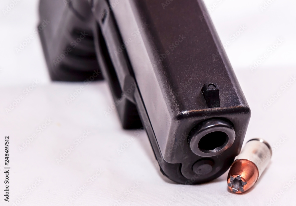 A black 9mm pistol shown with a single 9mm bullet on a white background A black 9mm pistol shown with a single 9mm bullet on a white background