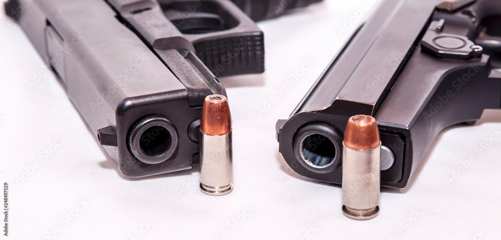 Two black pistols, a 9mm and a 40 caliber each with a bullet to it on front of the muzzle on a white background