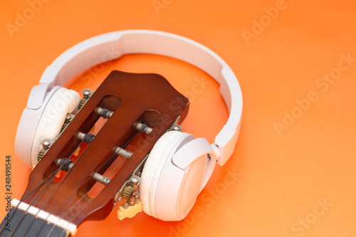 Wireless headphone on guitar on orange background. music concept, listen classical music