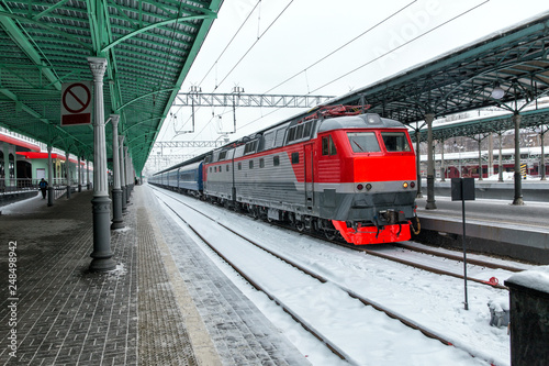 Electric locomotive and passenger train on railway in cold snowy winter day.