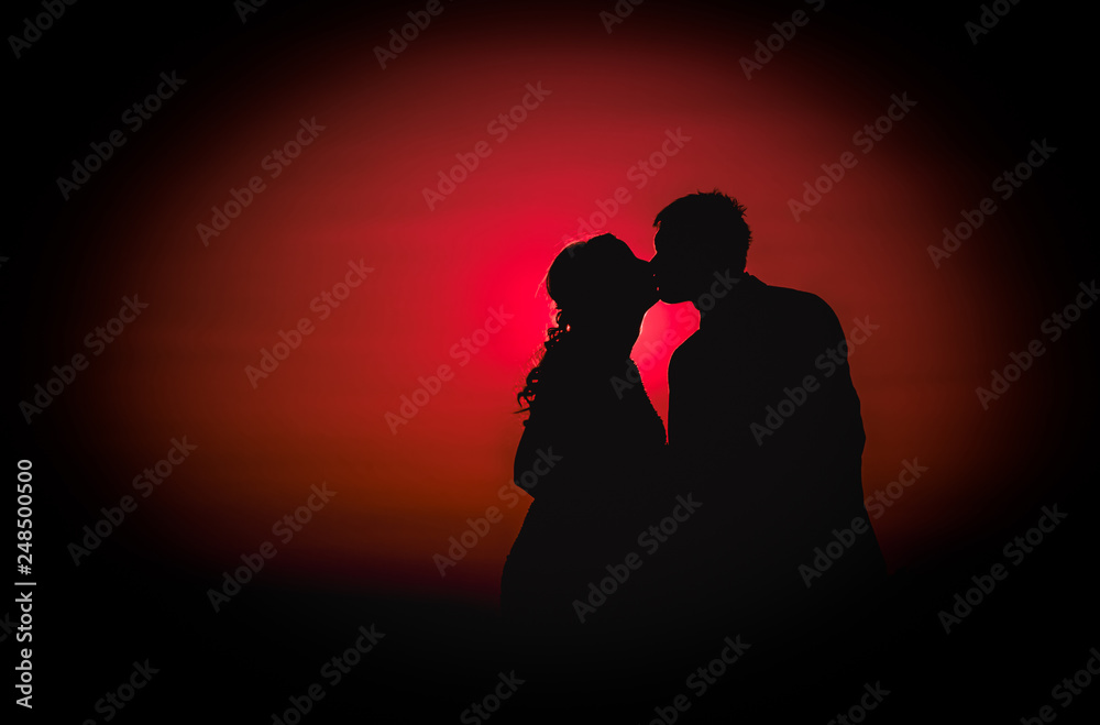 Silhouette photo of a young couple kissing at sunset on their wedding day - Red background
