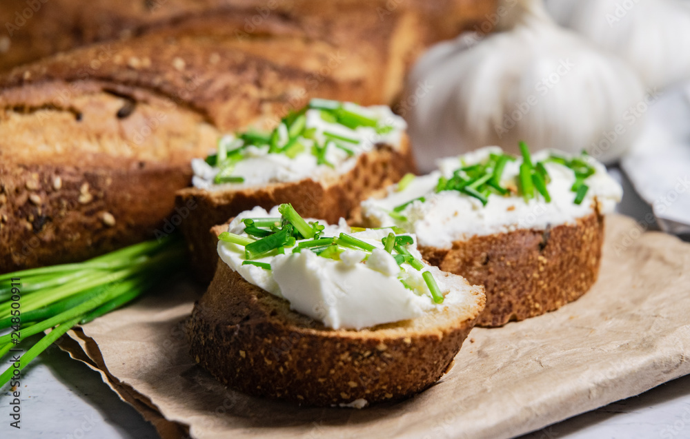 Pieces of French baguette with fresh green chives, white curd spread placed on rustic paper Pieces of French baguette with fresh green chives, white curd spread placed on rustic paper