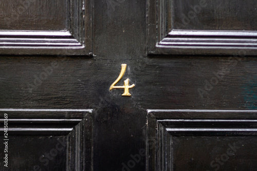 House number 4 in bronze as a numeral on a black wooden door