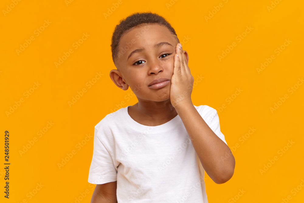 People, negative emotions, health and illness concept. Sad unhappy dark skinned male child having painful upset look, going to cry while suffering from intolerable toothache, touching chin People, negative emotions, health and illness concept. Sad unhappy dark skinned male child having painful upset look, going to cry while suffering from intolerable toothache, touching chin