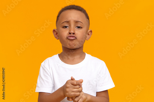 Picture for sad frustrated ten year old dark skinned child wearing white t-shirt pouting lips, having mournful facial expression, feeling sorry for misbehavior, asking parents not to punish him