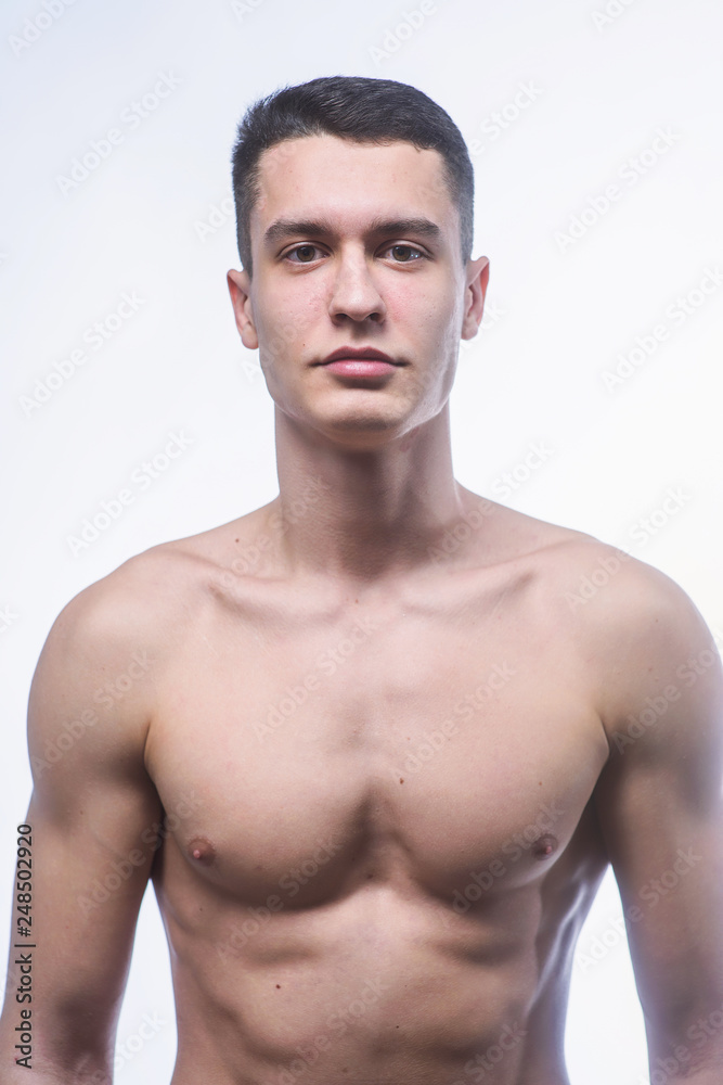 Beautiful young European athletic with bare torso, nice abs and muscles on white and gray background Beautiful young European athletic with bare torso, nice abs and muscles on white and gray background