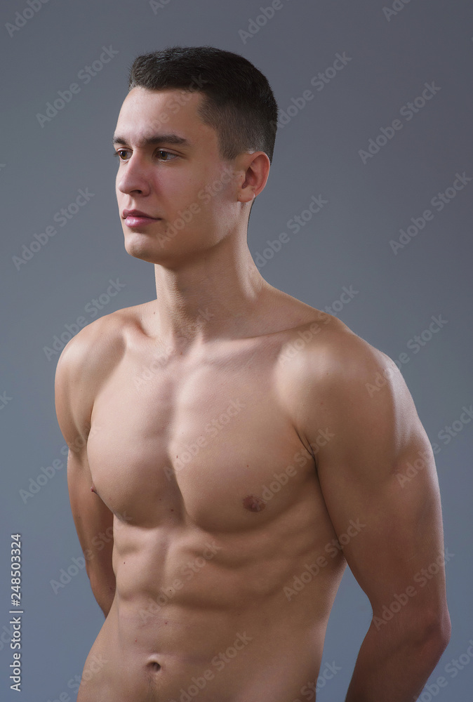 Beautiful young European athletic with bare torso, nice abs and muscles on white and gray background Beautiful young European athletic with bare torso, nice abs and muscles on white and gray background
