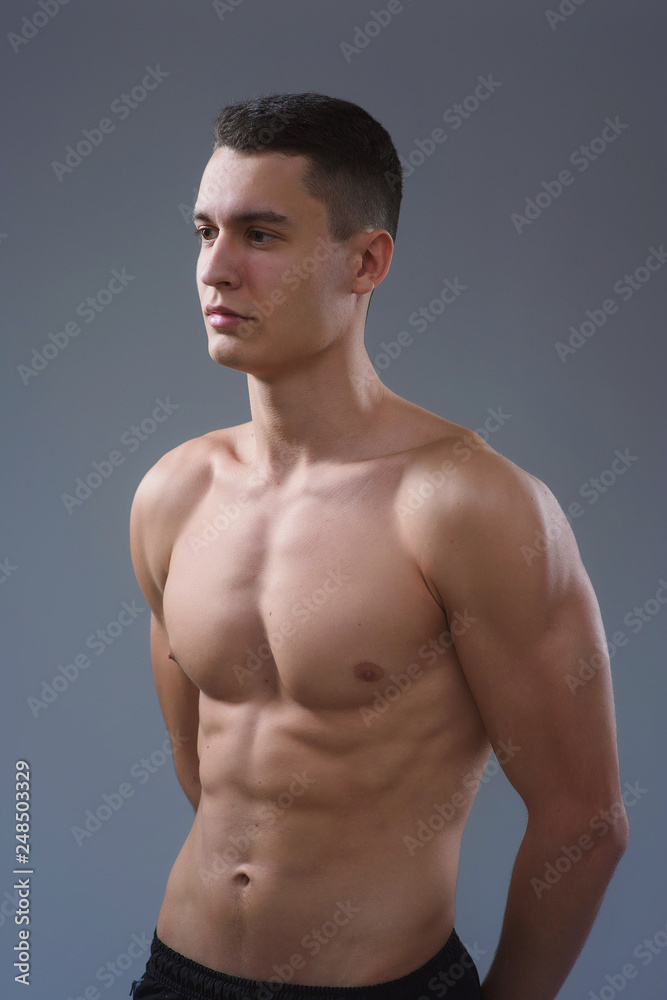 Beautiful young European athletic with bare torso, nice abs and muscles on white and gray background