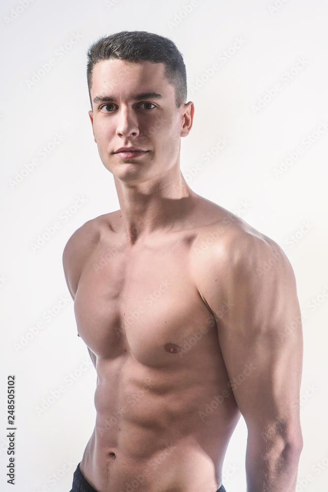 Beautiful young European athletic with bare torso, nice abs and muscles on white and gray background