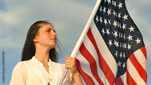 Serious girl teenager  stand with American flag against blue sky. Slow motion