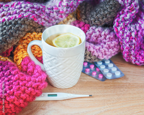 Concept of illness, colds, cure, fall and winter. Tea with lemon, thermometer, pills and a knitted blanket.