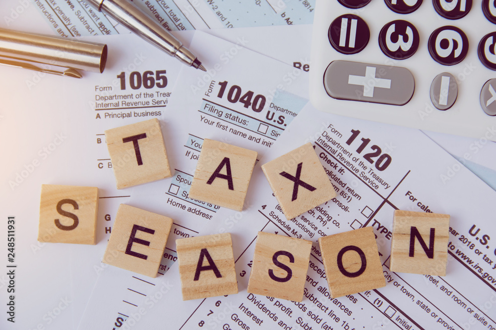 Tax season with wooden alphabet blocks, calculator, pen on 1040 tax form background Tax season with wooden alphabet blocks, calculator, pen on 1040 tax form background