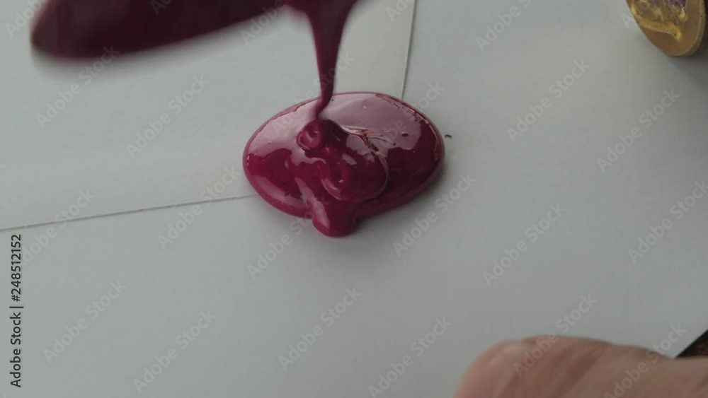 Closeup of man's hands sealing a letter with hot red wax and brass seal using the old medieval way
