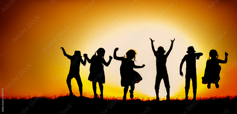 Silhouette of happy children boys and girls jumping and dancing in sunset sky evening time background as successful, happiness and careless concept